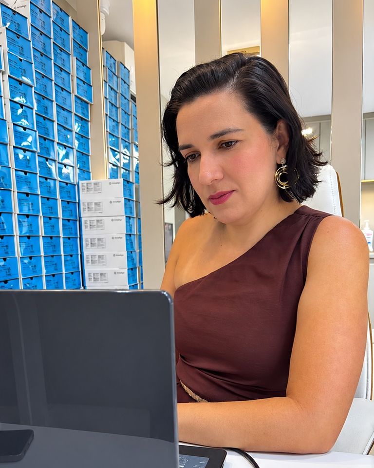 Dra. Alynne Macedo ao notebook no consultório, com caixas de alinhadores Invisalign ao fundo
