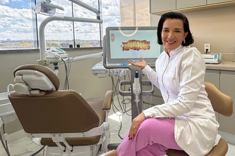 Dra. Alynne Macedo na sala de atendimento, ao lado do scanner iTero, com a janela ao fundo