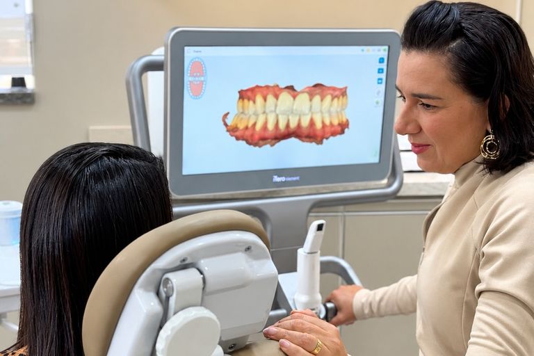Dra. Alynne Macedo ao lado da cadeira, com o scanner intraoral iTero e o modelo 3D da arcada na tela